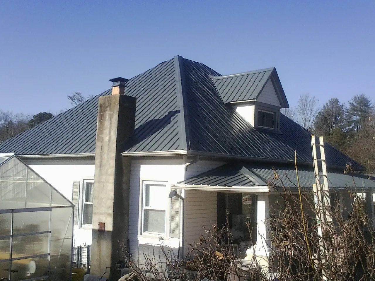 Dark blue standing seam metal roof on a white farmhouse with dormer — Slate & Tile Roof Repair by Roofing Brothers in Parma