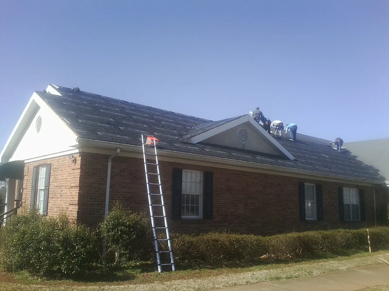 Crew tearing shingles off a brick ranch roof with a ladder set — Emergency Roof Repair work by our crew in Parma