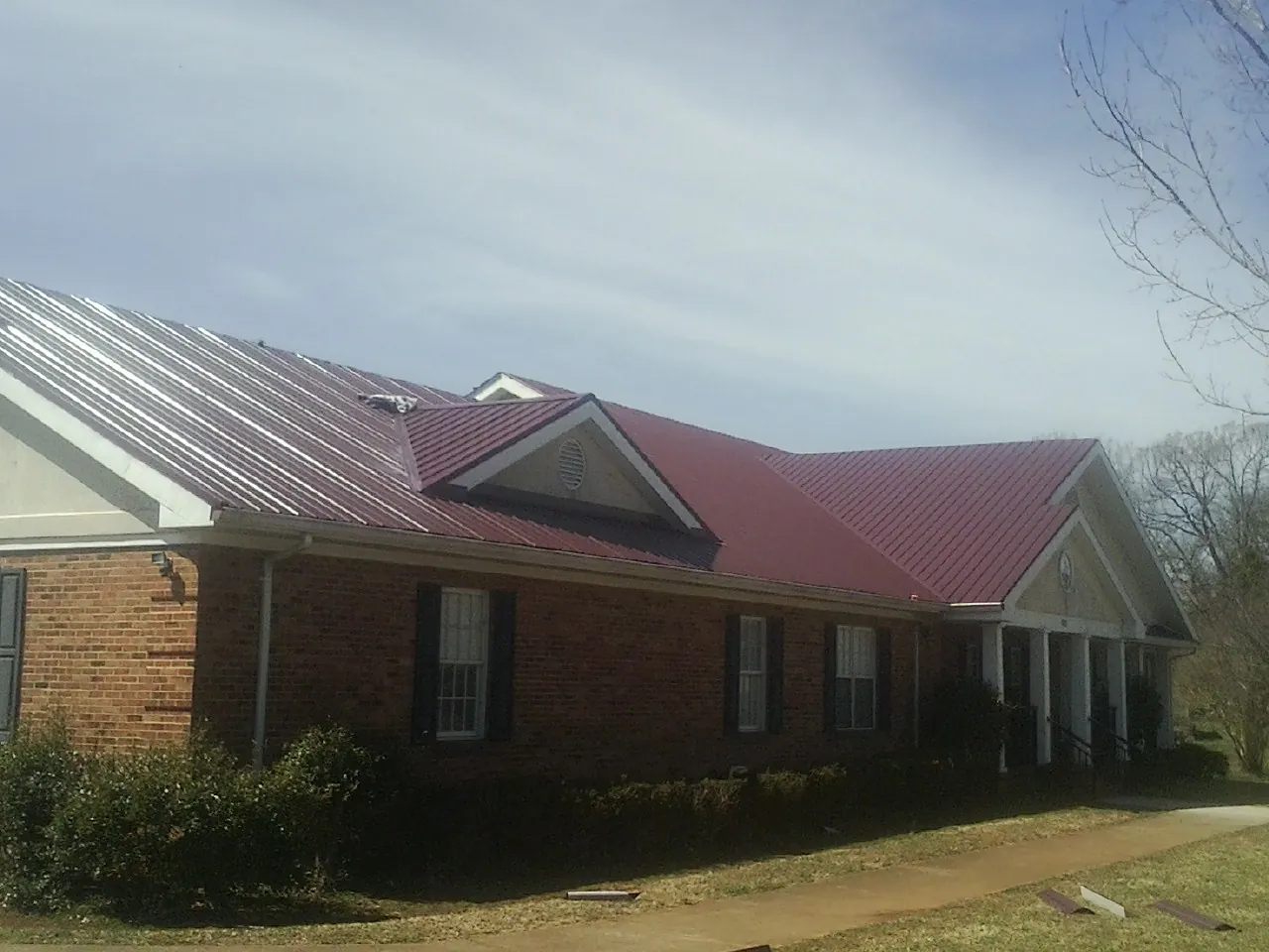 Red metal roof with gabled entries on a long brick building, from a Hail Damage Roof Repair job in Parma