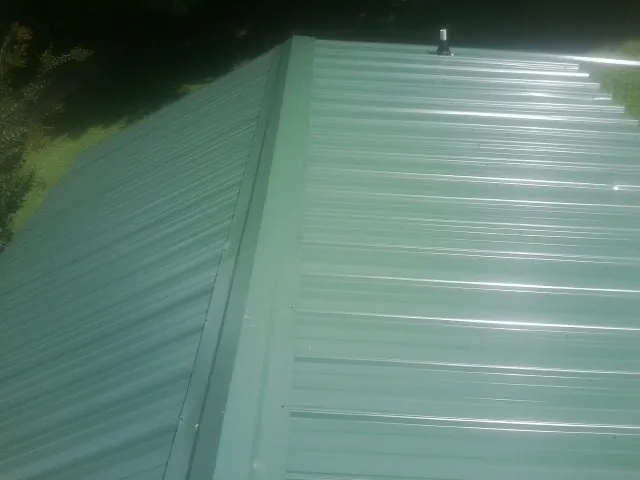 New green metal panels meeting at the ridge of a roof — Flat Roof Repair work by our crew in Parma