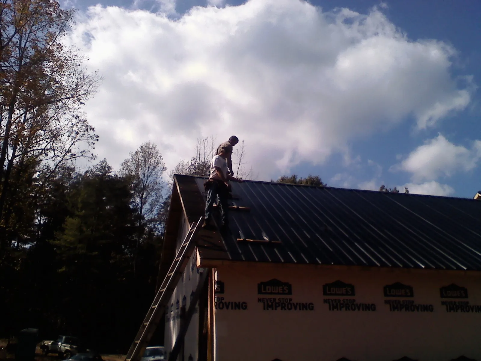 Roofer fastening dark metal panels high against a cloudy sky, from a Roof Inspection job in Parma
